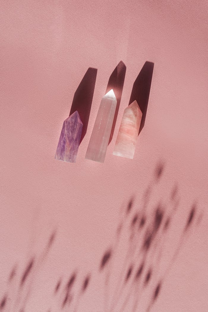 Three polished crystals casting shadows on a soft pink surface, creating a tranquil and mystical feel.